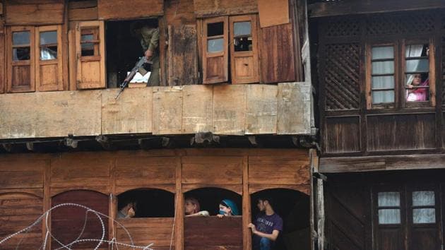 A security personnel stands guard inside a house as onlookers watch in Srinagar. (AFP Photo) A security personnel stands guard inside a house as onlookers watch in Srinagar. (AFP Photo)