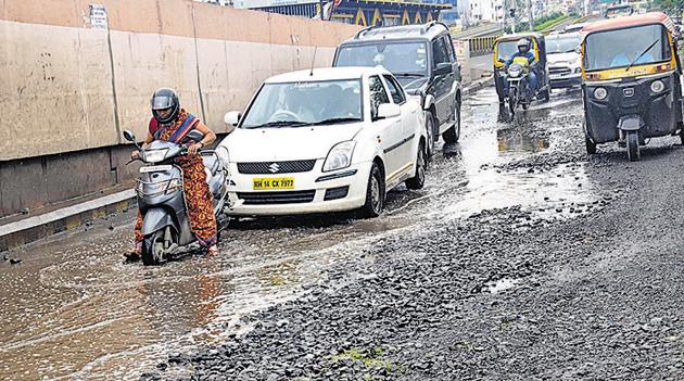 A two-wheeler rider struggles through a potholed stretch near Dange chowk.(HT PHOTO)