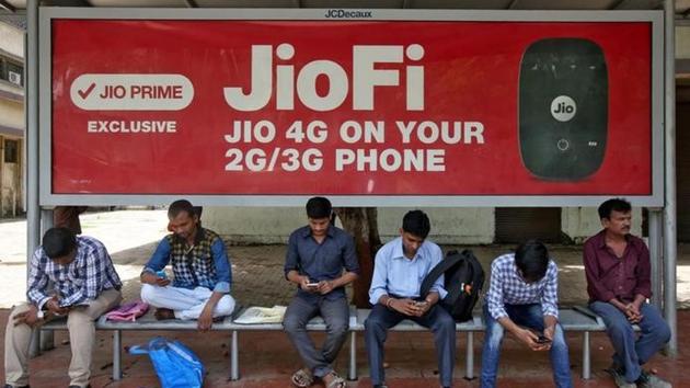 Commuters use their mobile phones as they wait at a bus stop with an advertisement of Reliance Industries' Jio telecoms unit, in Mumbai.(Reuters Photo)