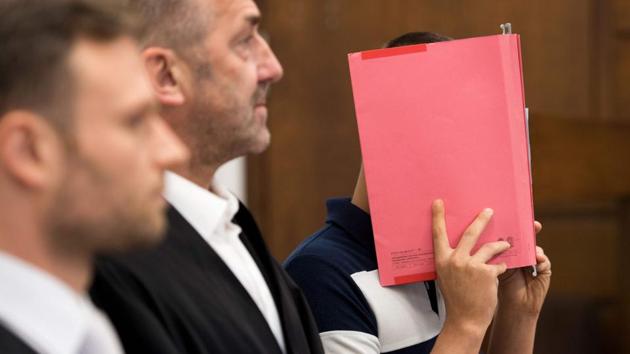 Picture taken on July 21, 2017 shows a 29-years-old defendant hiding his face behind a folder as he stands next to his lawyers at a courtroom in Cologne, western Germany. (AFP) Picture taken on July 21, 2017 shows a 29-years-old defendant hiding his face behind a folder as he stands next to his lawyers at a courtroom in Cologne, western Germany. (AFP)