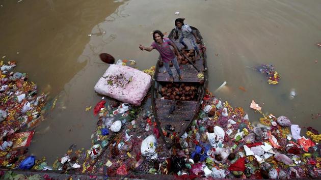 Men wade through religious offerings and immersed idols by the bank of the Sabarmati river which cuts through Ahmedabad, to collect coconuts and other reusables thrown by devotees. (PTI)