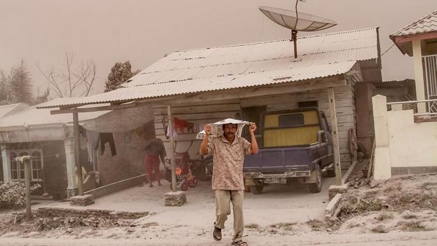 A villager covers his head as thick ashes blankets Tiga Pancur village in Karo. (IVAN DAMANIK / AFP)