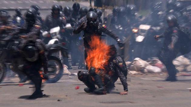A police officers helping a colleague who caught fire after an explosive device went off as they rode past during a protest against the elections for a Constituent Assembly in Caracas. Deadly violence erupted around the controversial vote, with a candidate to the all-powerful body being elected shot dead and troops firing weapons to clear protesters in Caracas and elsewhere. (Leo RAMIREZ / AFP)