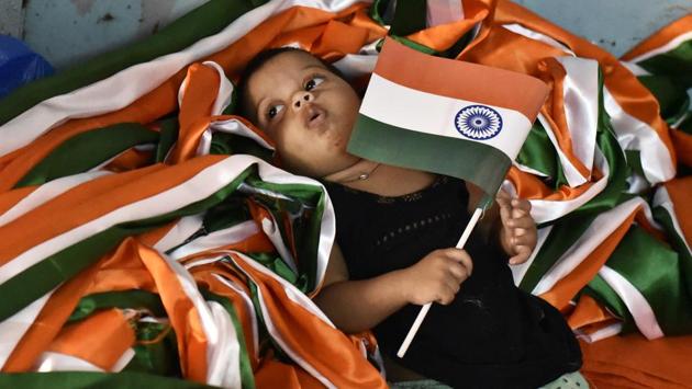 A little girl holds on to a national flag, laying in a heap of tricoloured ribbon as other family members are busy completing orders at a flag making workshop in Old Delhi. (Burhaan Kinu / HT Photo)