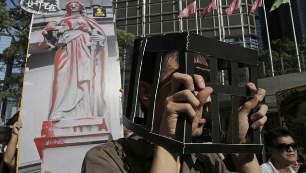 Protesters wearing the uniform of prisoners and raise a poster with an image of Statue of the Goddess of Justice during a rally to support young activists Joshua Wong, Nathan Law and Alex Chow in downtown Hong Kong on August 20, 2017.(AP Photo)