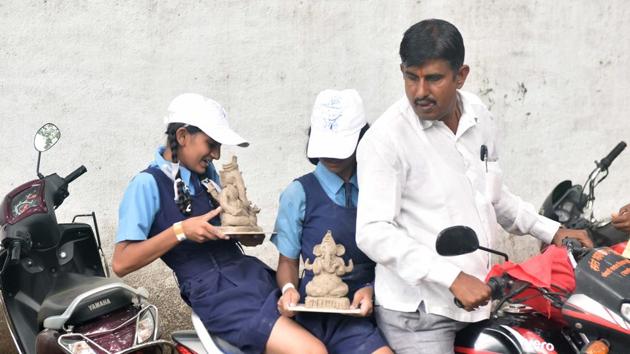 A girl tries to ensure that the Ganesh idol she made does not collapse while sitting pillion on a scooter. (Pratham Gokhale/HT PHOTO)