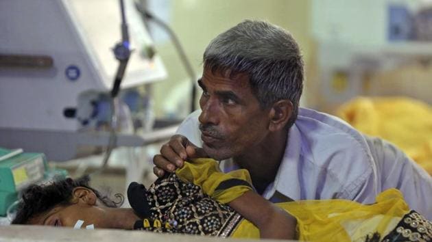 A family member attends to a child receiving treatment at the state-run Baba Raghav Das Medical College Hospital in Gorakhpur, Uttar Pradesh. Acute encephalitis syndrome is a catch-all term to describe patients suffering fever, vomiting, headaches and brain function issues such as confusion, trouble speaking and coma along with seizures.(AP File Photo)