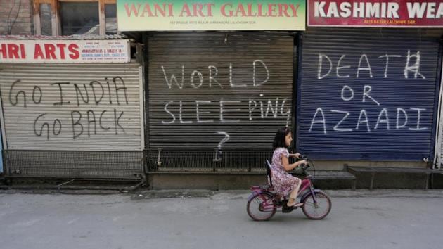 A girl rides past closed shops during a shutdown in Srinagar on August 12. (HT File)