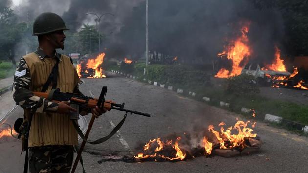 Security personnel looks at burning vehicles set alight by rioting followers of Dera Sacha Sauda chief Gurmeet Ram Rahim Singh convicted of rape in Panchkula on August 25.(AFP Photo)