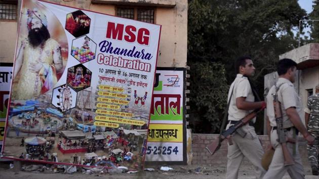 Policemen walk past a poster of Ram Rahim while patrolling a street in Sirsa after the announcement of jail sentence for the Dera chief on Monday.(PTI Photo)