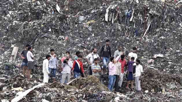 People stand atop a garbage landfill after part of it collapsed in Ghazipur area on Friday.(HT Photo)