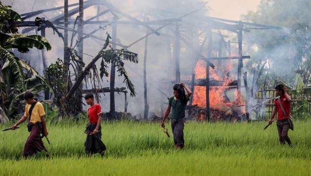 Unidentified men carry knives and slingshots as they walk past a burning house in Gawdu Tharya village near Maungdaw in Rakhine state in northern Myanmar on September 7.(AFP Photo)