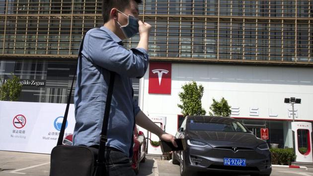 In this file photo, a man wears a mask walks past a Tesla electric vehicle showroom and charging station in Beijing, China. (AP Photo) In this file photo, a man wears a mask walks past a Tesla electric vehicle showroom and charging station in Beijing, China. (AP Photo)