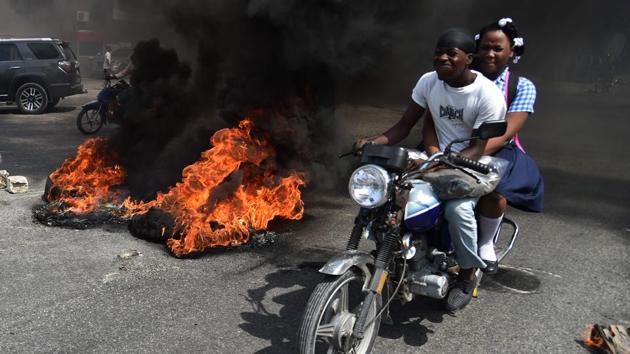 A couple on a motorcycle drive past burning tires placed by demonstrators on a main road in the Haitian capital Port-au-Prince, on September 12, 2017. Demonstrators took to the streets to protest against the government and the new budget for 2018, throwing stones at the police, setting tires on fire and blocking some streets. (Hector Retamal / AFP) A couple on a motorcycle drive past burning tires placed by demonstrators on a main road in the Haitian capital Port-au-Prince, on September 12, 2017. Demonstrators took to the streets to protest against the government and the new budget for 2018, throwing stones at the police, setting tires on fire and blocking some streets. (Hector Retamal / AFP)
