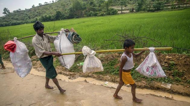 A Rohingya Muslim boy, Mohammad Arafat, carries his belongings and walks with his father Zahoor Hussain as they arrive at Taiy Khali refugee camp, Bangladesh, Thursday, September 21, 2017.(AP Photo)
