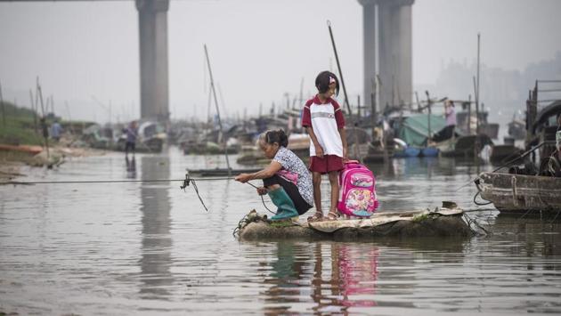 On a morning in Datang, an older woman in rubber boots squatted on a small bank as she pulled in a fishing line. Beside her, a girl stood in a red and white uniform, holding onto a pink Disney princess backpack. Jumping from a boat to the sandy shore, she began her walk to school. (Fred Dufour / AFP)