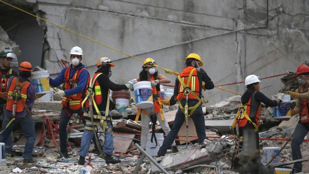 Search and rescue workers remove rubble a bucket at a time while standing on the debris of a felled office building brought down by a 7.1-magnitude earthquake, in the Roma Norte neighborhood of Mexico City, Sunday, Sept. 24, 2017.(AP)
