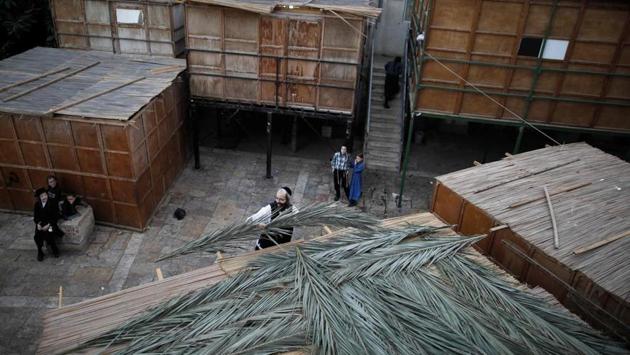 A Jewish man lays palm branches on the roof of a temporary hut. During the period of the festival, people eat and sleep in these makeshift booths with the first day being Shabbat (rest day) in which work is forbidden. (Menahem Kahana / AFP)