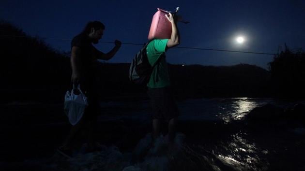 A local resident carries a gasoline can as he crosses a river using a cable in San Lorenzo. One other villager, dependent on dialysis treatment, was placed in a water barrel and pushed across the river by his neighbours. (Alvin Baez / REUTERS)