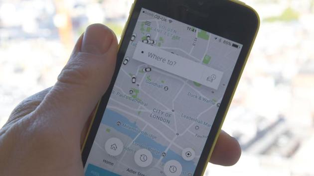 A man posing whilst holding a smartphone showing the App for ride-sharing cab service Uber in London on September 22. (AFP File Photo)
