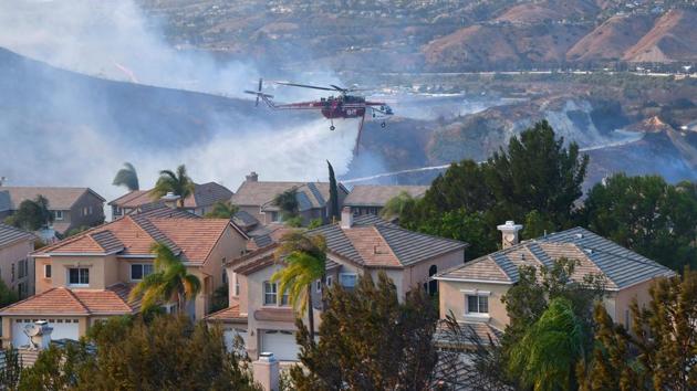 A helicopter drops water near homes at the Anaheim Hills neighborhood in Anaheim, California after a fire spread quickly through the area prompting mandatory evacuations and freeway closures. (AFP Photo)