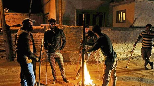 A group of vigilantes stand by fire as they carry out a night-long vigil against alleged incidents of ‘braid chopping’ in their area on the outskirts of Srinagar.(Waseem Andrabi/ HT Photo)