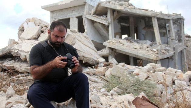 A picture taken on October 10, 2017, shows Syrian photographer Ahmed Khatib checking his pictures next to damaged building in the village of Marayan in the Idlib province.(AFP Photo)