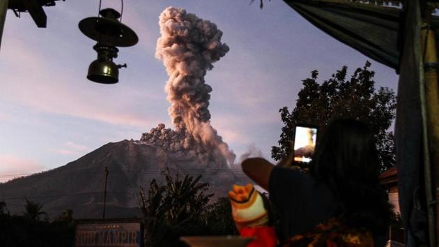 An Indonesian villager takes a picture of Mount Sinabung volcano as it spews thick smoke as seen from Tiga Pancur village in Karo, North Sumatra on October 17, 2017. (Ivan Damanik / AFP)