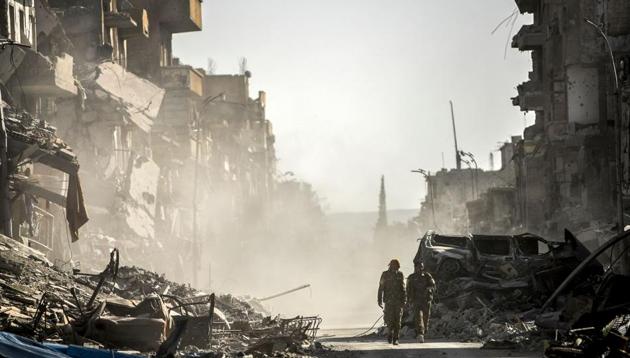 (FILES) This file photo taken on October 20, 2017 shows fighters of the Syrian Democratic Forces (SDF) walking down a street in Raqa past destroyed vehicles and heavily damaged buildings after a Kurdish-led force expelled Islamic State (IS) group fighters from the northern Syrian city, formerly their "capital". (AFP) (FILES) This file photo taken on October 20, 2017 shows fighters of the Syrian Democratic Forces (SDF) walking down a street in Raqa past destroyed vehicles and heavily damaged buildings after a Kurdish-led force expelled Islamic State (IS) group fighters from the northern Syrian city, formerly their "capital". (AFP)