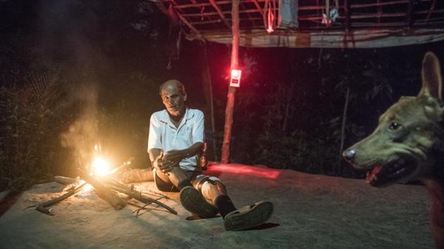 Chandu Jadhav, a tribal leader at Aarey and Vanicha Pada resident keeps vigil by lighting a fire outside his home. His dog Tommy stays by his side and has been attacked by leopards multiple times. The settlements have always shared space with big cats, but every night the kuccha roads here are deserted, doors locked and windows tightly shut. The silence is broken only by the growl of a predator making its way through villages in search of food. (Satish Bate / HT Photo)