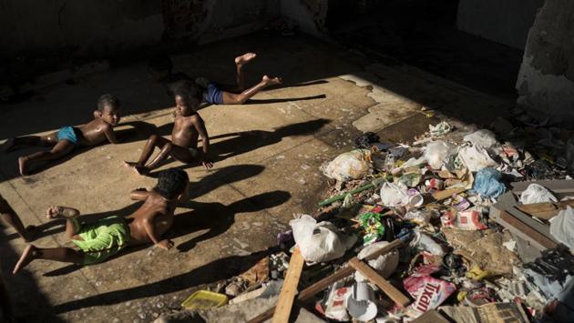 Children slide on a puddle near trash as they play in a squatted building. Hundreds of destitute residents living in the building find food by rummaging through garbage illegally dumped in the area. (Felipe Dana / AP)