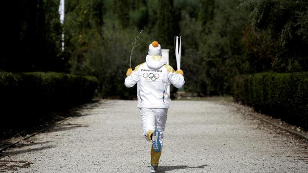 The first torchbearer Greek skier Apostolos Angelis runs with the Olympic flame and an olive branch at the Pierre de Coubertin monument during ceremony. This long torch relay will culminate with the 2018 Winter Olympics opening on 9 February 2018. (Alkis Konstantinidis / REUTERS)