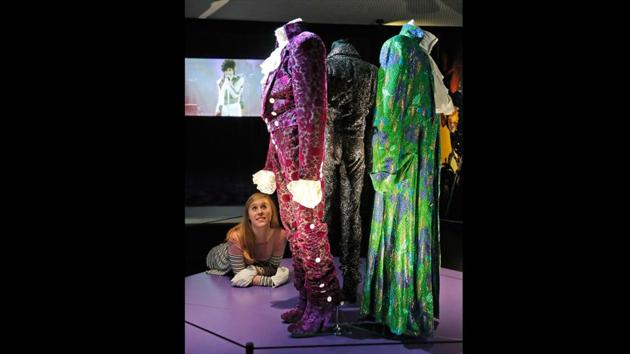 An employee looks at costumes once worn by the performer and pop icon Prince at the exhibition. For visitors, it is a unique insight into the life, creativity and vision of one of the most naturally gifted recording artists whose sudden death last year shook the world. (Frank Augstein / AP Photo)