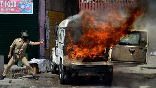 A policeman stands next to a police vehicle set ablaze by protesters in Anantnag district of South Kashmir .(PTI file photo)