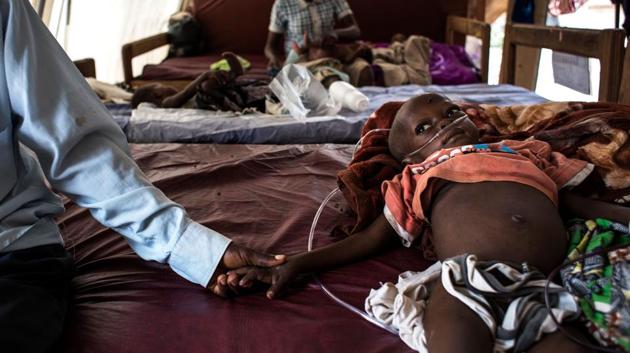 A father holds his severely malnourished child's hand, on his bed inside a feeding and rehabilitation centre on October 23, 2017 in Tshikapa. Conflict in the Kasai Provinces between the local militia, Kamwina Nsapu and Government troops have displaced 1.4 million people since August, 2016. (John Wessels / AFP)