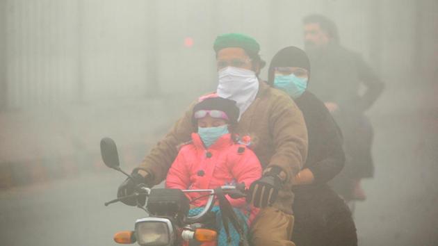 People use face masks to protect themselves from morning smog as they ride on bike along a road in Lahore on Friday.(REUTERS photo)