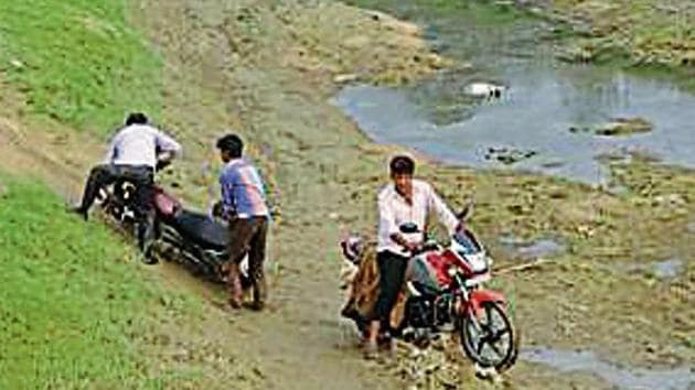 Locals struggle to cross the dry river bed with their motorcycles in Uttar Pradesh’s Birahimpur village.(HT Photo)