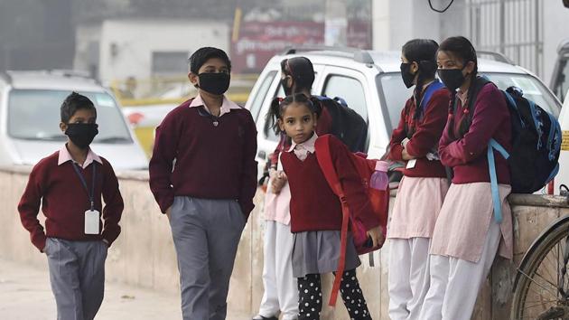 Children wearing masks wait for their school bus in New Delhi on Monday. (PTI) Children wearing masks wait for their school bus in New Delhi on Monday. (PTI)