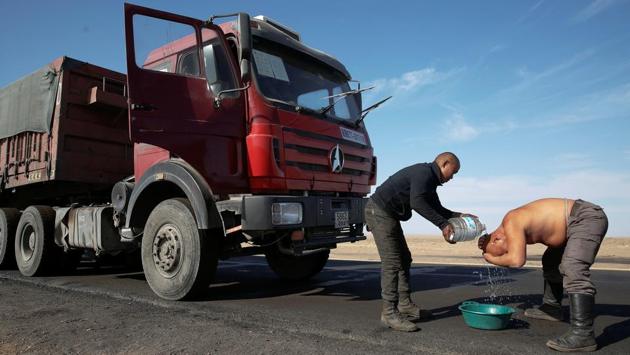 A truck driver washes himself with bottled water on the highway for delivering coal to China at Khangobd Soum in the Gobi desert, Mongolia. This serpentine crawl towards the border can take up to a week. (B. Rentsendorj / Reuters)