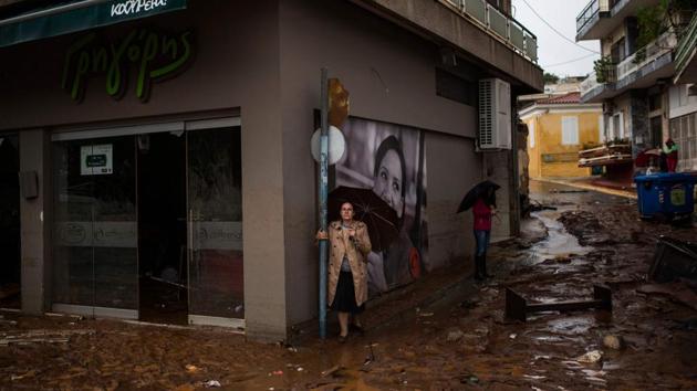 Women holding umbrellas stand next to a damaged shop, in a flooded street of Mandra, northwest of Athens on November 15, 2017. At least seven people died and more were missing after a strong overnight downpour flooded three towns in Greece, officials said. (Angelos Tzortzinis / AFP) 