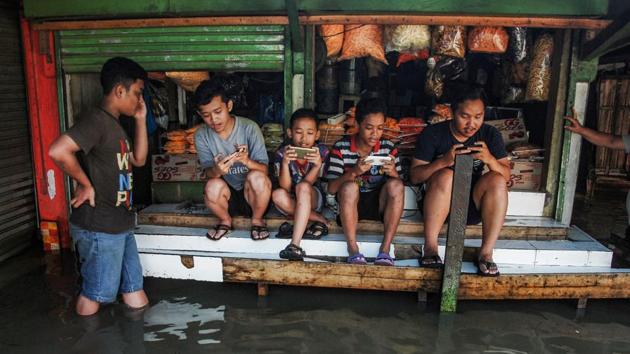 Indonesian youths sit on a table while playing games at a game centre surrounded by floodwaters after seasonal rains hit the area around Bandung, West Java province on November 17, 2017. (Timur Matahari / AFP) 