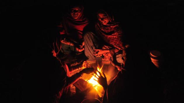 People warm themselves around a bonfire on a cold winter morning at Dwarka.(HT File)