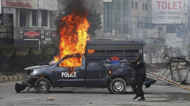 A Pakistani police officer aims his gun towards the protesters next to a burning police vehicle during a clash in Islamabad on November 25. (AP photo) A Pakistani police officer aims his gun towards the protesters next to a burning police vehicle during a clash in Islamabad on November 25. (AP photo)