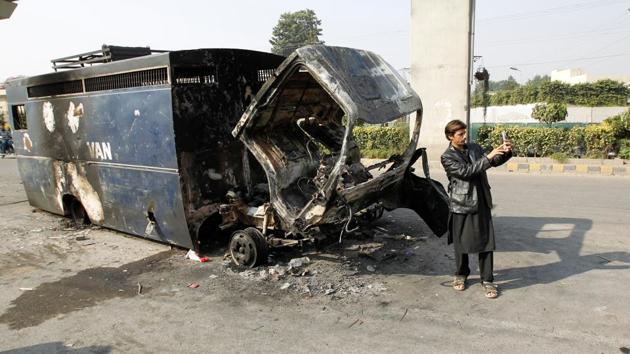 A passerby takes a selfie in front of a police prison van destroyed during clashes with police near the Faizabad junction in Islamabad on Sunday.(Reuters) A passerby takes a selfie in front of a police prison van destroyed during clashes with police near the Faizabad junction in Islamabad on Sunday.(Reuters)