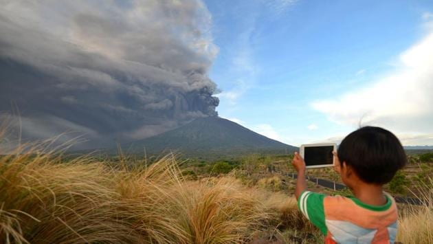 A boy takes pictures during Mount Agung's eruption seen from Kubu sub-district in Karangasem Regency on November 26, 2017 in Bali, Indonesia. Mount Agung belched smoke as high as 1,500 metres above its summit, sparking an exodus and air traffic shutdowns on the tourist island. (Sonny Tumbelaka / AFP)
