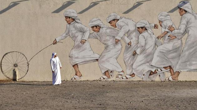 A man walks past a giant mural depicting boys running after a wheel in traditional Arab garb on November 30, 2017 in Dubai, United Arab Emirates. (Giuseppe Cacace / AFP)