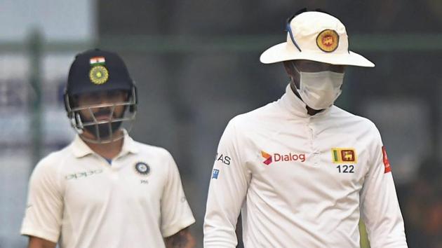 Sri Lanka cricket team captain Dinesh Chandimal wears an anti-pollution mask as Indian cricket team skipper Virat Kohli looks on during the second day of the third Test at Ferozeshah Kotla in New Delhi on Sunday.(PTI)