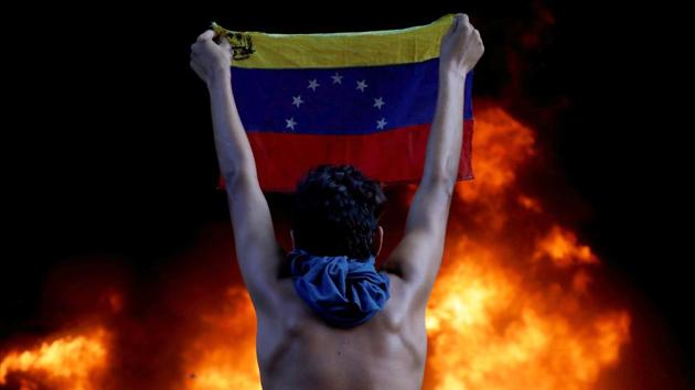 A protestor holds a national flag facing a fire at the entrance of the Supreme Court, during a rally against President Nicolas Maduro, in Caracas, Venezuela on June 12, 2017. Going into a fourth year of crippling recession, Venezuela’s 30 million people found themselves skipping meals, suffering shortages of basic foods and medicines, unable to keep up with dizzying inflation, and emigrating in ever larger numbers. (Carlos Garcia Rawlins / REUTERS) A protestor holds a national flag facing a fire at the entrance of the Supreme Court, during a rally against President Nicolas Maduro, in Caracas, Venezuela on June 12, 2017. Going into a fourth year of crippling recession, Venezuela’s 30 million people found themselves skipping meals, suffering shortages of basic foods and medicines, unable to keep up with dizzying inflation, and emigrating in ever larger numbers. (Carlos Garcia Rawlins / REUTERS)