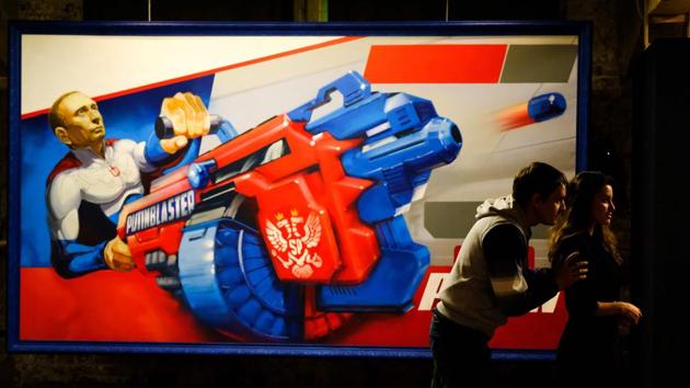 Visitors stand next to a painting depicting a stoic Vladimir Putin brandishing a “Putin Blaster” at the exhibition. Hailed by allies as a leader who has restored national pride and expanded Moscow’s international clout, no challenger appears capable of unseating the leader at the moment. (Yuri Kadobnov / AFP)