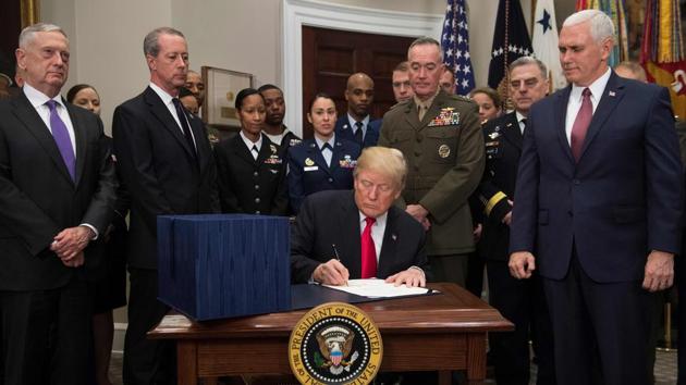 US President Donald Trump, surrounded by military officials and members of Congress, signs the National Defense Authorization Act for Fiscal Year 2018 at the White House in Washington, DC, on Tuesday. (AFP)